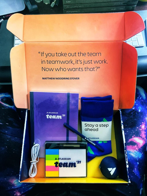 a swag box from Atlassian Team ‘21 with a notebook, pen, pair of socks, stickies with multi-USB ports, and a stress ball.