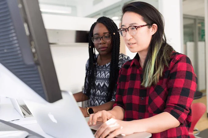 two women looking at a shared screen, along with their two laptops