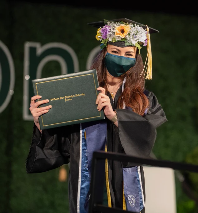 A female graduate with a crown of flowers stops for a photo. 