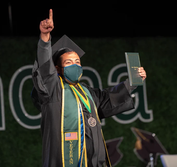 A male veteran graduate celebrates as he receives his diploma during the drive-in commencement ceremonies. 