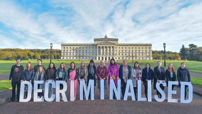 Women in Northern Ireland stand outside Stormont with a sign that says "Decriminalised"