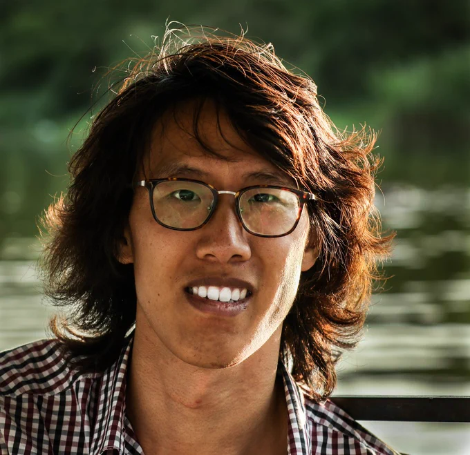 A man smiling, wearing a plaid shirt and glasses.