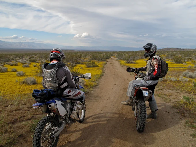 Two individuals wearing motorbike safety equipment on a riding trail. 