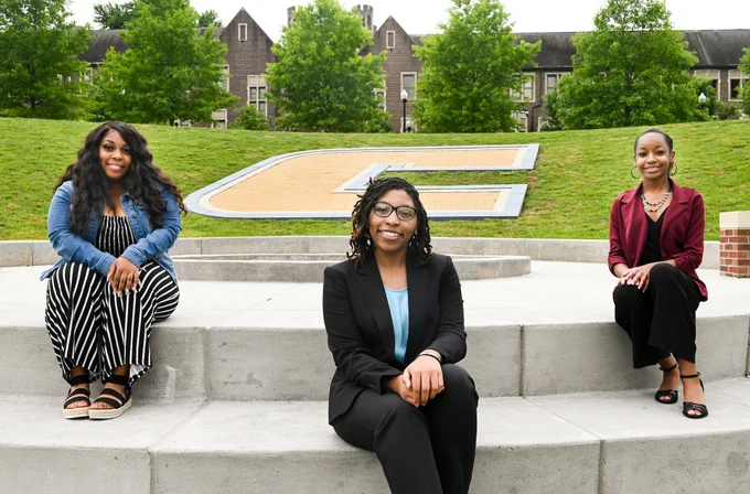 Three students spread out in front of the Power C logo at Chamberlain Field.