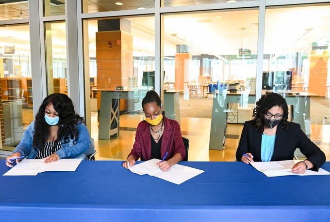 Three students signing their letter of intents to participate in a scholarship program for Education majors at the University.
