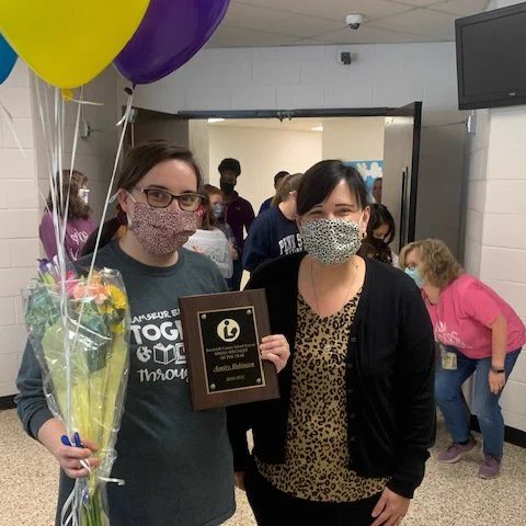 Media specialist Amity Robinson with Director of Digital Teaching and Learning Shenna Creech standing in a hallway with balloons and flowers. She is holding an award for Media Specialist of the Year.