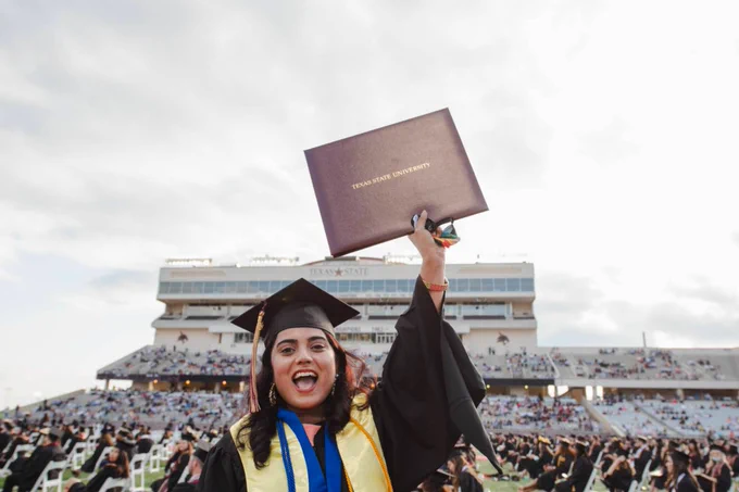 Texas State University Bobcat Stadium Spring 2021 Graduation Smiling Student Raising Diploma