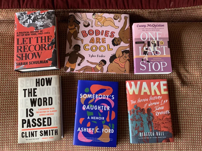 Six different books on a red and gold plaid ottoman. Let the Record Show by Sarah Shulman; Bodies are Cool by Tyler Feder; One last stop by Casey McQuiston; how the word is passed by Clint Smith; somebody’s daughter a memoir by Ashley C Ford; and wake the hidden history of women lead slave revolts by Rebecca Hall