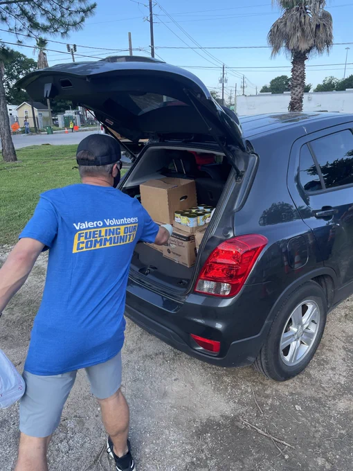 An employee wearing a Valero Volunteers shirts drops food in a trunk