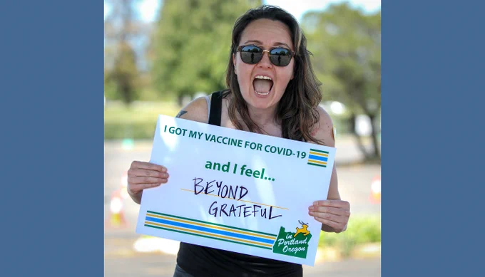 Emma stands outdoors holding a sign with an excited smile! Emma’s sign says: “Today I got my COVID-19 vaccination and I feel beyond grateful, because these people are volunteering and giving up their time to make sure that I can get what I need and that our community can go back to normal life. And I'm completely overwhelmed with gratitude for the government who has worked to get us to this point, for the scientific researchers, everybody who's been involved. It's been an enormous effort.”
