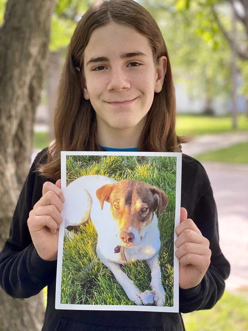 Gideon outside holding a picture of a white dog with a brown head (Watson) lying on his belly in the grass.