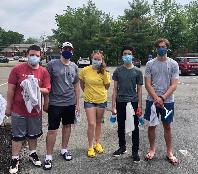 Photo of five students from the Washingtonville High School senior class, holding car wash supplies during a fundraiser.
