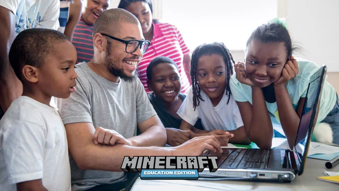 A group of students clustered around a teacher working on Minecraft: Education Edition on a laptop.