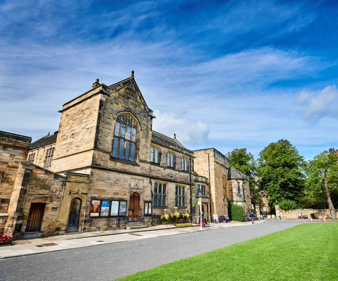 Palace Green Library, Durham. A stone brick nineteenth century building with ornate windows, and posters for exhibition events outside.