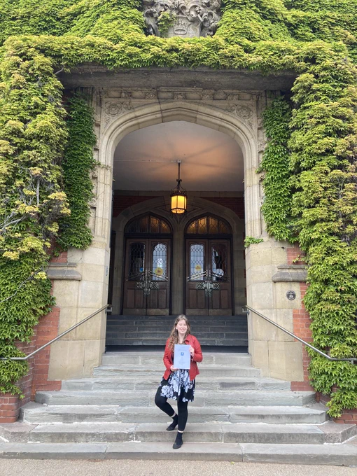 Jen stood in front of a university building holding her dissertation