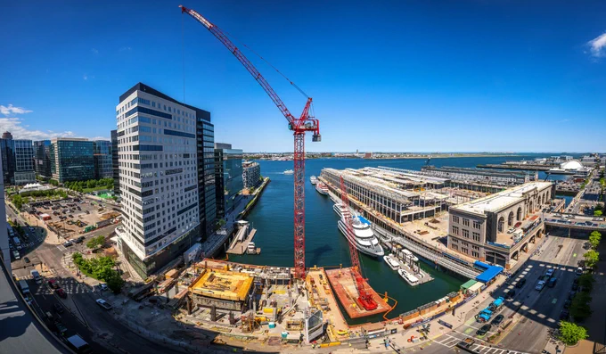 An aerial panoramic shot looking down at the site of The St. Regis Residences, Boston, with a red crane towering over a construction site along Boston Harbor