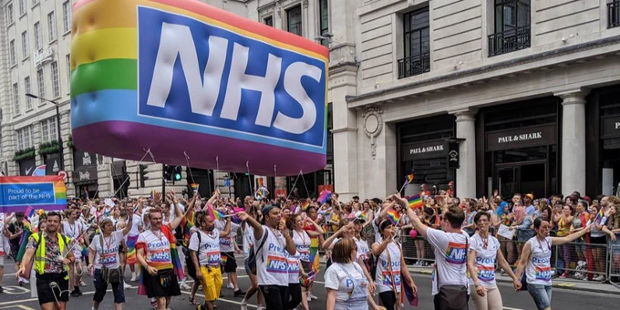 NHS staff walk in front of a large rainbow NHS logo at Pride parade