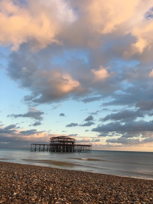A photograph of the West pier and Brighton beach with low tide, cloudy skies and the sun setting