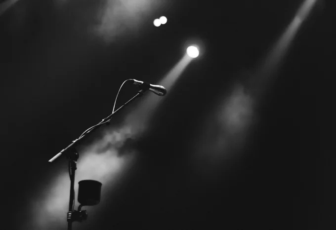 Black and white photo of a microphone stand on a stage with lights