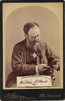 Portrait of man with long beard seated in a chair. He’s not looking at the camera. He’s holding something and looking down at it, probably a notebook. Text: Wilkie Collins. 680 Broadway. 
