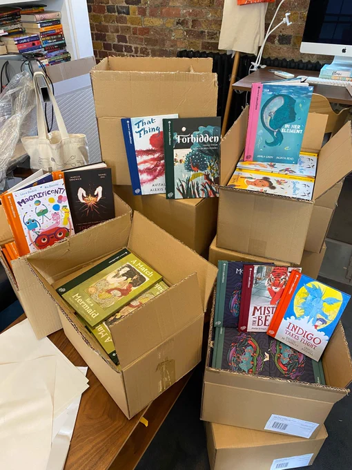 A stack of open boxes filled with hardback books, with other books propped up against them