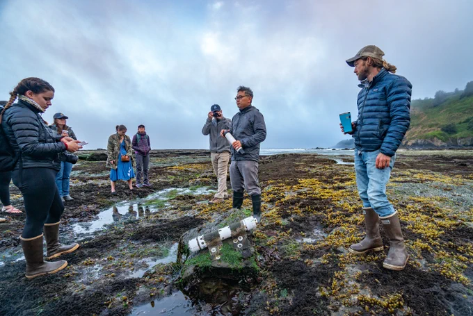 A group of people stand on Oregon's rocky coast, discussing ocean acidification. 
