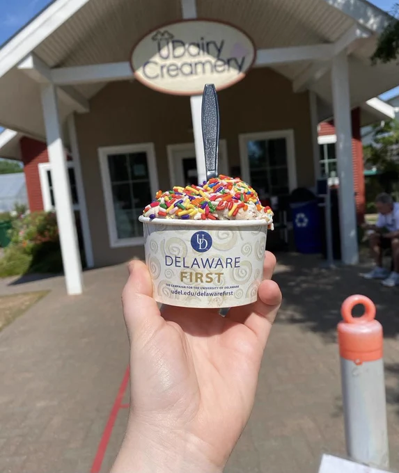 Student holds a cup of UDairy ice cream with sprinkles in front of the UDairy building on campus.