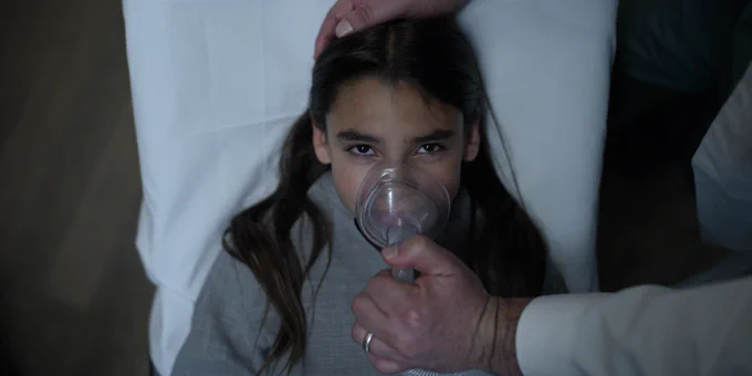 Ariana Greenblatt's character in "Awake" being given oxygen in a hospital bed.