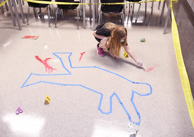 female student working around an outline of a body on the floor