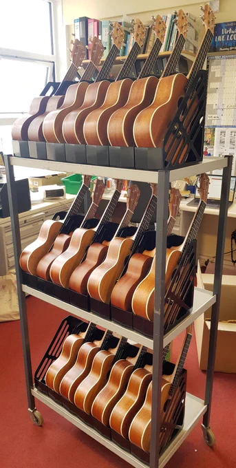 A three-tier cart on wheels. Each tier has seven magazine files in a row, each of which contains a ukulele.