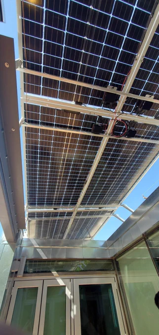 A black set of solar panels is photographed from below. Behind the panels a clear blue sky is visible.
