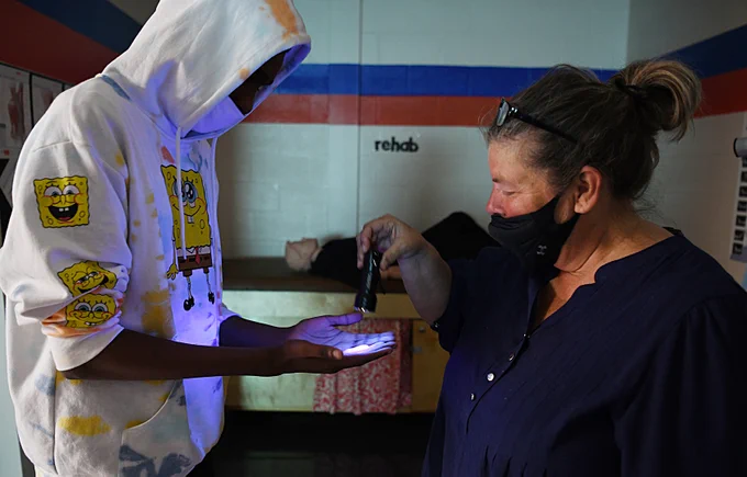 teacher holding black light to student's hands.