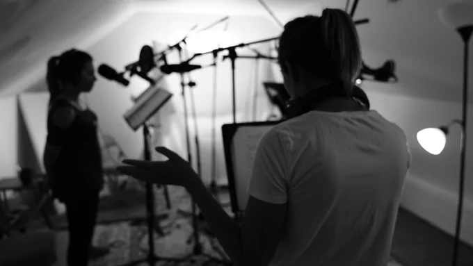 ID: A black and white photo of Windfall co-writer Christie Donato as she directs Clare Lopez and Mallory Roach during season one production.