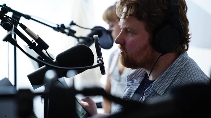 ID: a color photo of Josh Rubino performing as Captain Root during the recording of Windfall season one.