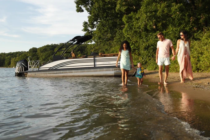 Family walking on the beach by a Harris Solstice Pontoon Boat