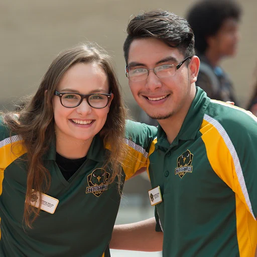 Two student life ambassadors pose for a photo in matching green & gold polos. 