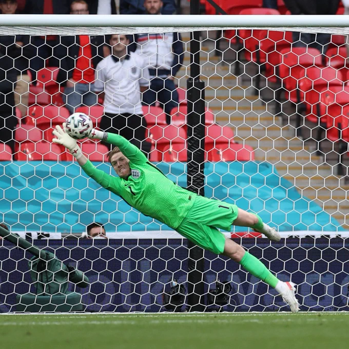 Jordan Pickford in all green England kit making a double handed full length save, diving away to his right