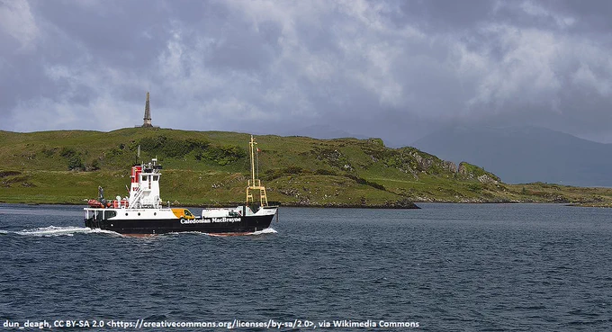 A small car ferry passes a headland upon which there is a large stone obelisk 
