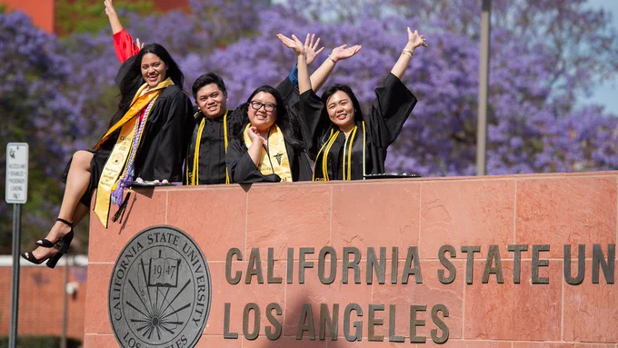 Celebrating grads in caps and gowns on Cal State LA sign