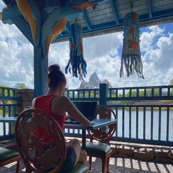 Girl working on laptop under pavilion on the water with view of Expedition Everest at Disney’s Animal Kingdom