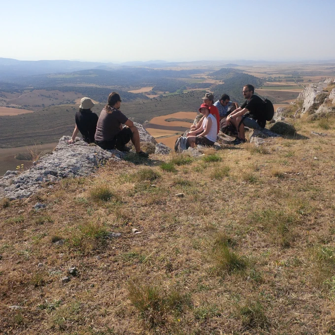 Un grupo de personas sentados en el suelo, al borde de un risco. Al fondo se ven los infinitos campos de Castilla.