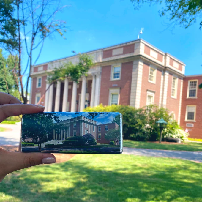 Hand holding a chocolate bar with a photo of a library, the same library is in the background of the photo creating a visual illusion