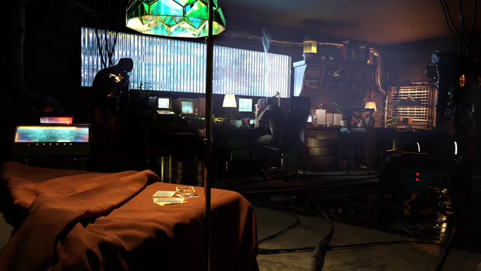 A women sits alone in the dark at her desk. Her and the cloud of smoke above her are illuminated by a future cityscape. There are scattered robot pieces around her and an unmade bed.