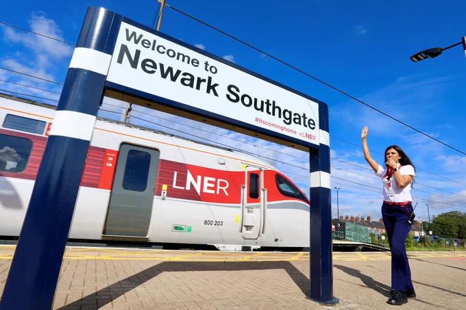 An LNER Azuma with a member of staff, and a sign that says 'Welcome to Newark Southgate #itscominghome @LNER'