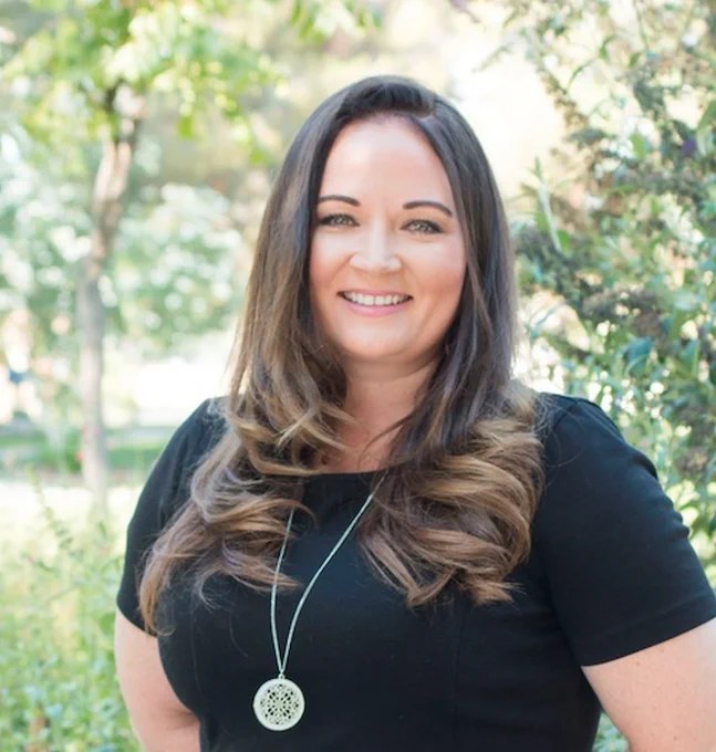 Portrait of woman smiling outdoors with greenery behind her. 