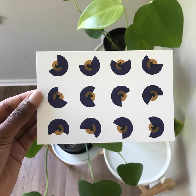 A picture of me holding a print in front of a backdrop of plants. The print is of arcs of circles of various radii coming together to make 12 distinct circle. Each circle is composed of three arcs: blue, yellow, and green. 