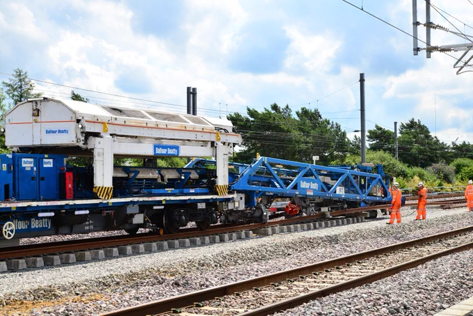 The track laying train lowering sleepers to the ballast on the ground and laying the steel rails in place over them.