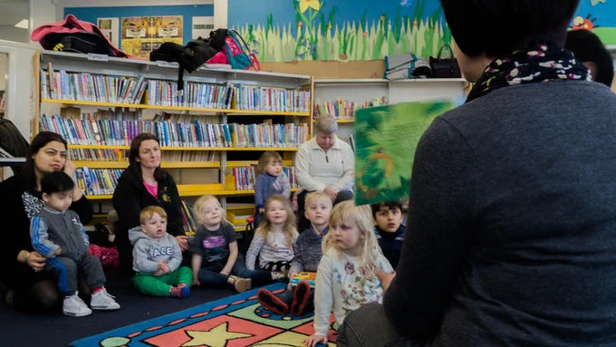 A group of children and their parents listen a storyteller in a library