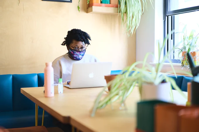 sashoy wears a facemask sitting at a desk with a laptop and plants