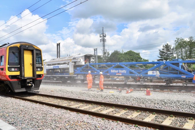 Engineers install the new railway track at Werrington as an East Midlands Railway train passes in front.